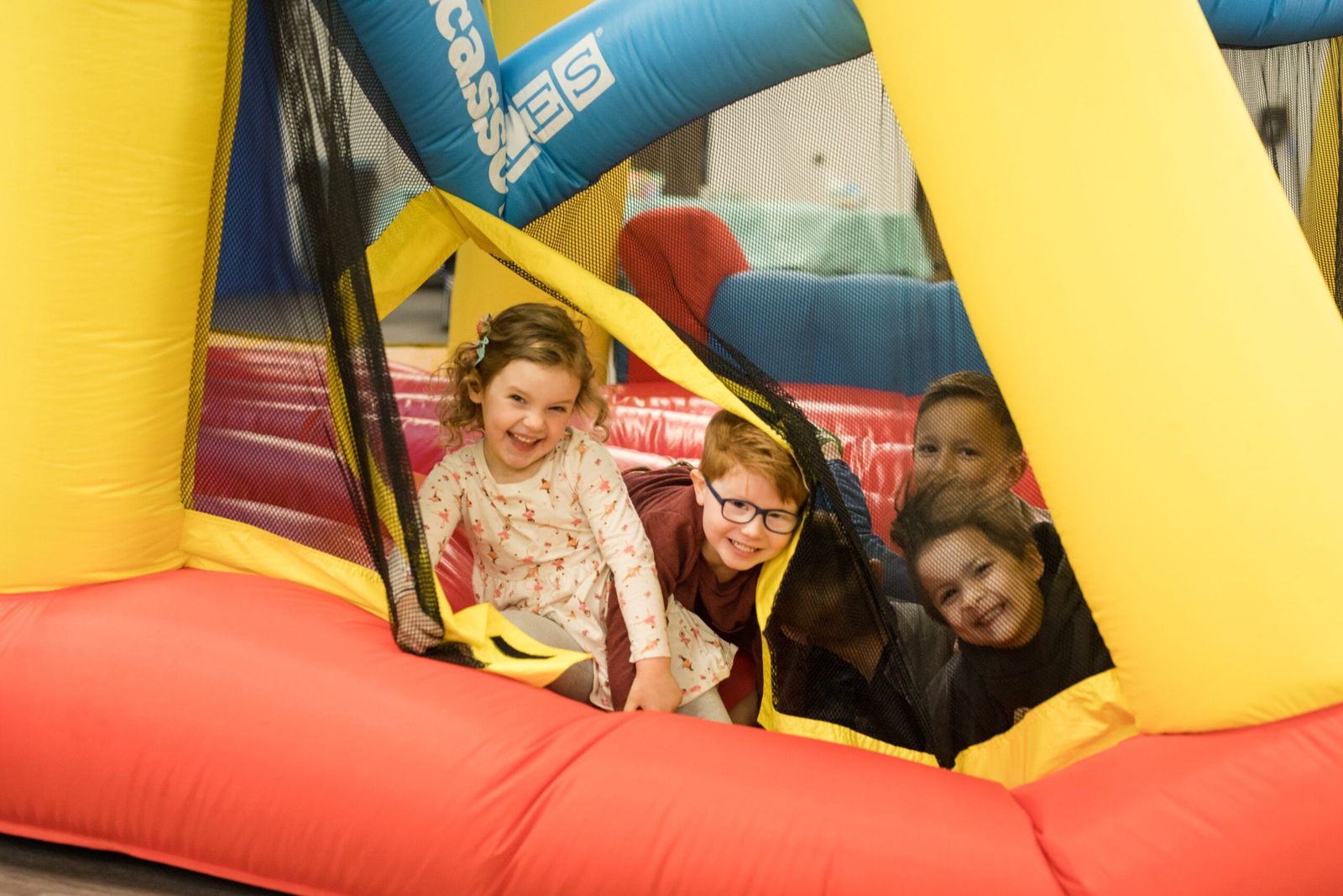 Three children grinning inside an inflatable bounce house at a kids event.