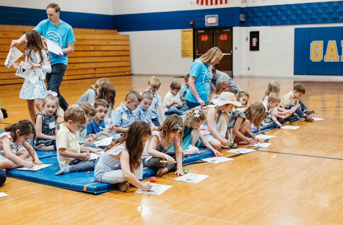 A leader teaching a large group of kids sitting on the gym floor.
