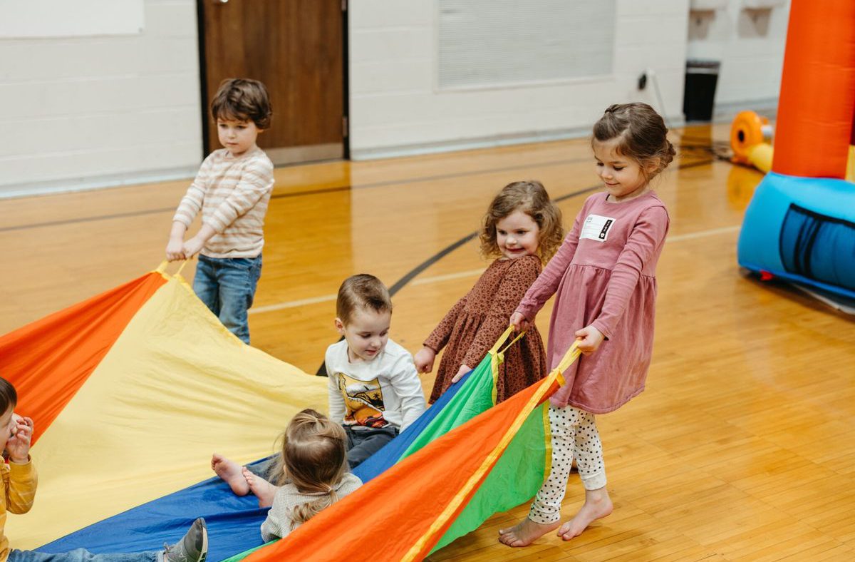 Preschoolers playing under a rainbow parachute.